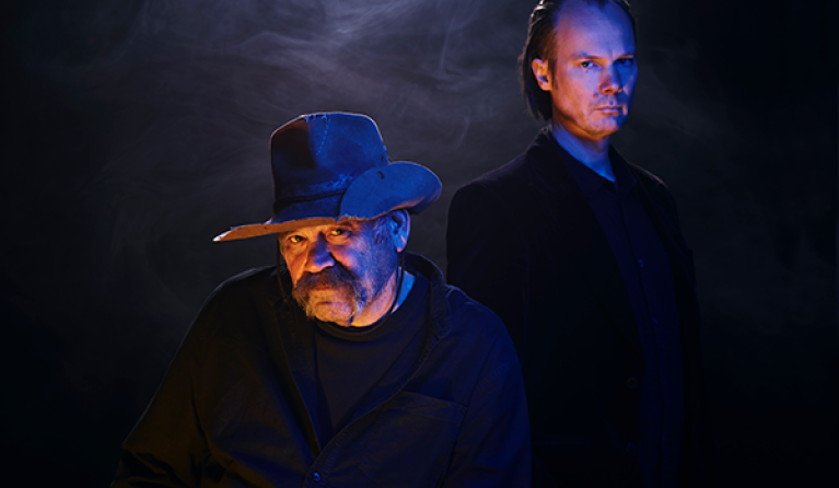 Two men in shadows look at the camera