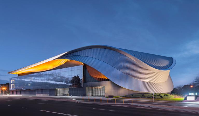 The external view of the Bunjil Place precinct from the road - a large, sweeping metal gridshell across two stories of windows.
