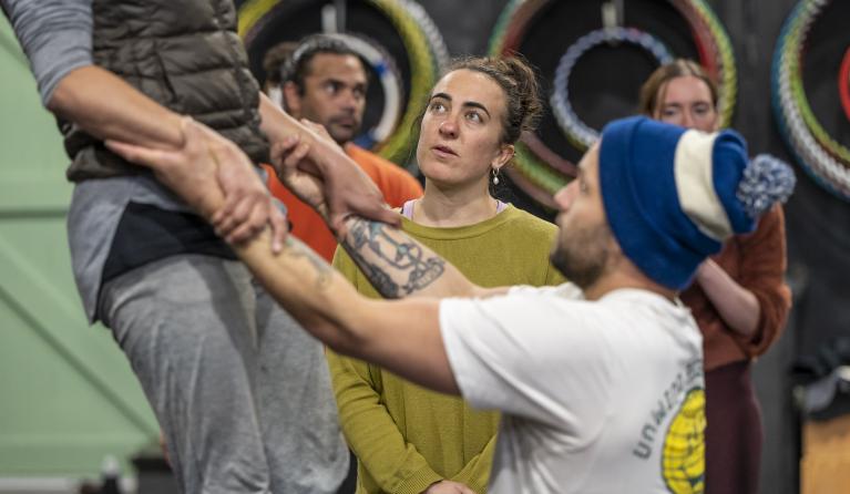 A man lifts up another watched on by other circus performers