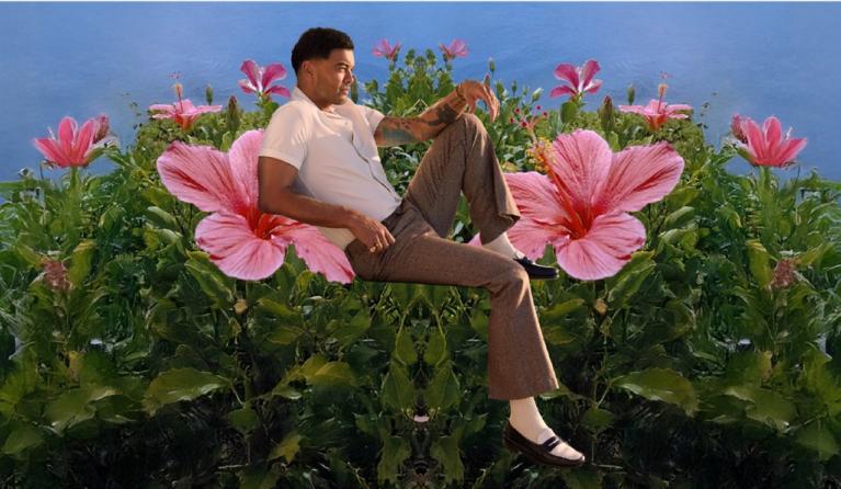 A man in a white shirt and tan pants sits amongst large flowers
