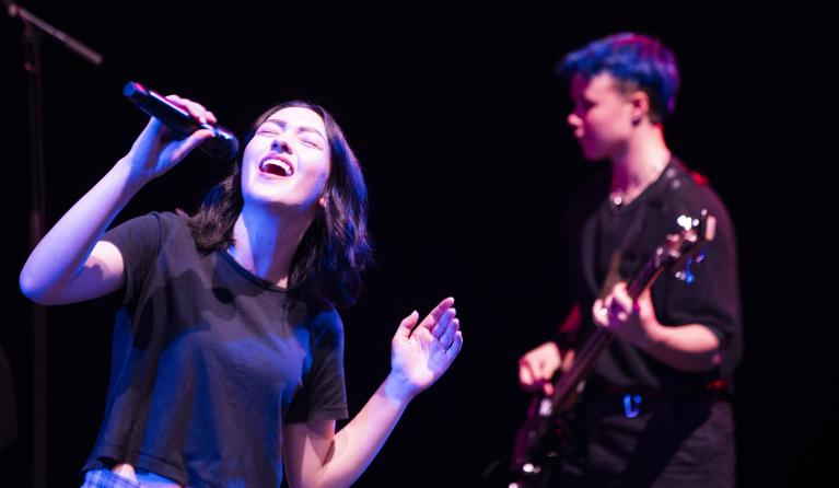 two student band performers, one with a microphone the other playing the electric guitar