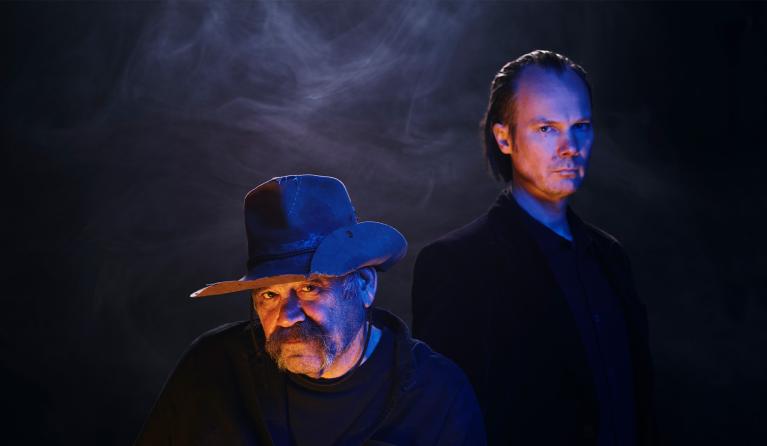 Two men in shadows look at the camera