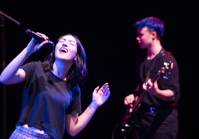 two student band performers, one with a microphone the other playing the electric guitar