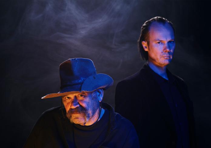 Two men in shadows look at the camera