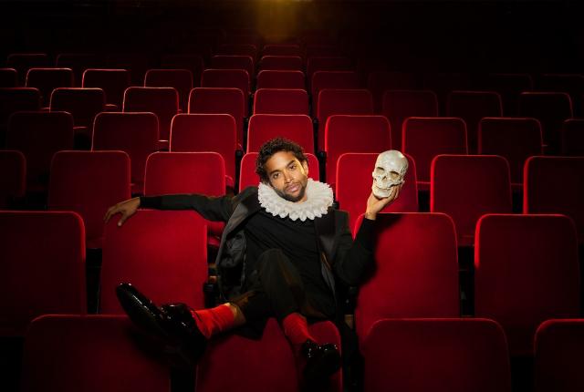 A man sits in a theatre holding a skull. 