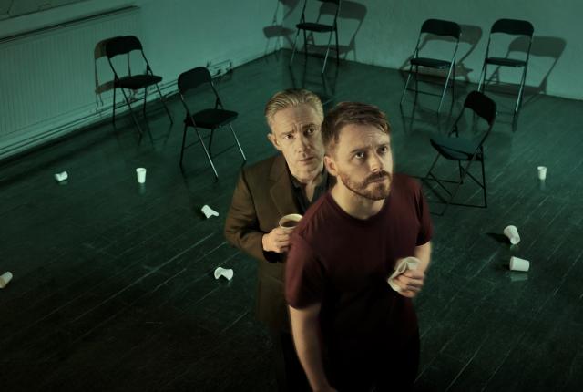 Two men stand in a room, looking up at a security camera