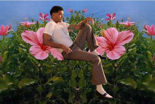A man in a white shirt and tan pants sits amongst large flowers