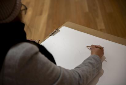 person wearing grey jacket sketching on white paper using a grey lead pencil