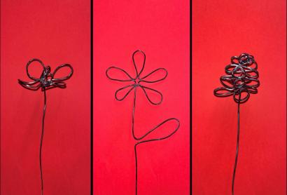 Three pieces of wire shaped like flowers, against a red background.
