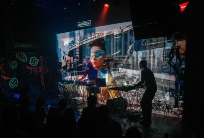 Two men DJing in front of a large screen with a crowd watching
