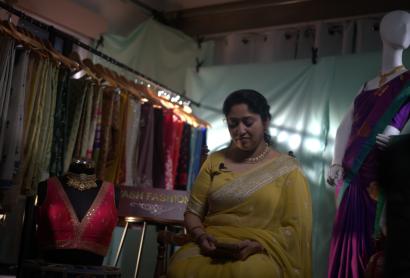 a woman in a yello sari sitting next to a display of many colourful saris