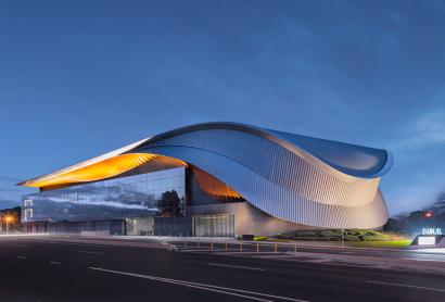 The external view of the Bunjil Place precinct from the road - a large, sweeping metal gridshell across two stories of windows.